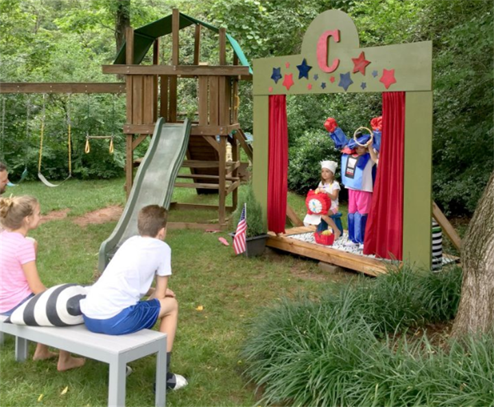DIY backyard kids theater stage with red curtains, children staging a puppet show on the lawn
