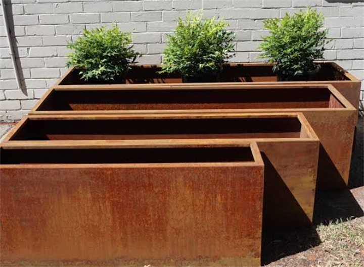 Stack of empty long rectangular Corten steel weathering steel planters against white brick wall