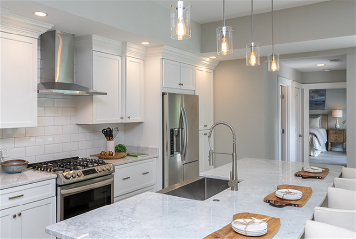 Completed luxury kitchen with white cabinetry, marble island countertop, stainless steel appliances and pendant lighting
