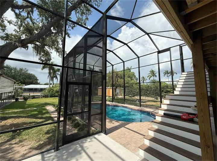 Gable-style aluminum pool screen cage with entry door, circular swimming pool and tropical Florida landscaping