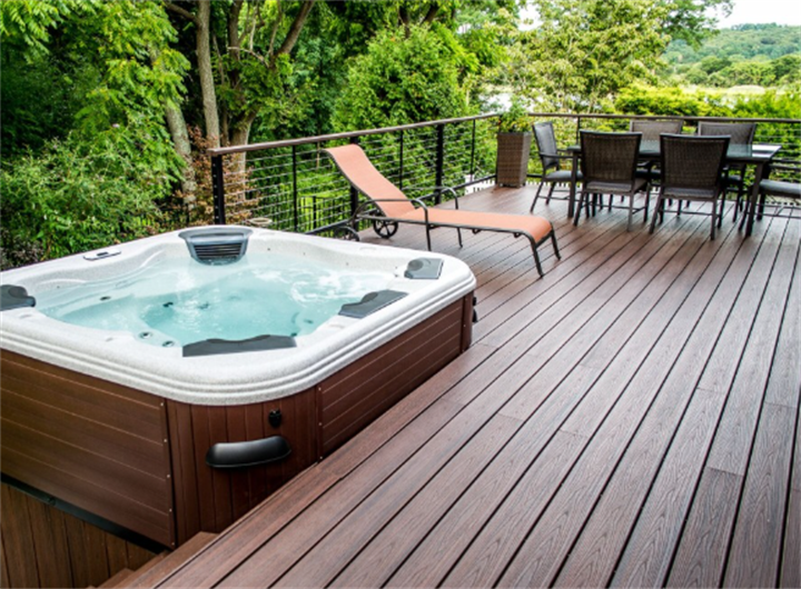 Freestanding hot tub on elevated backyard deck surrounded by lush green woodland