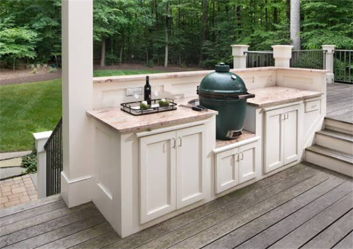 White built-in outdoor kitchen with kamado grill constructed on elevated wooden deck slope